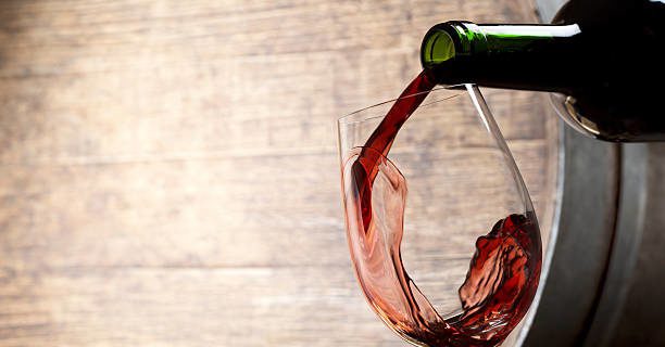 Un verre à pied est rempli par le goulot d'une bouteille de vin rouge avec un mouvement du vin en panaché dans le fond du verre.